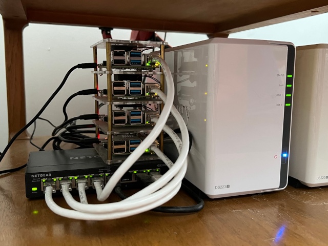 A stack of Raspberry Pi machines on top of a network switch next to two NASes